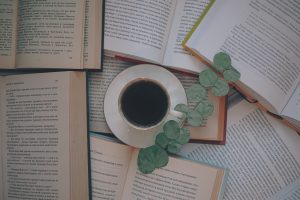 image of books with coffee on a table open with a cup of coffee in the middle and a lead of eucalyptus